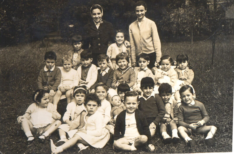 Fotografía en blanco y negro de un grupo de niños y niñas junto a sus maestras