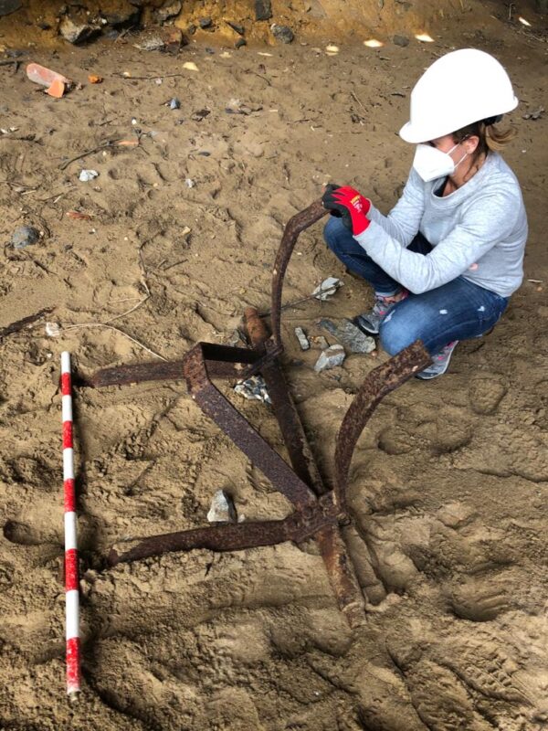 Mujer arqueóloga midiendo una pieza de metal en un lugar arenoso