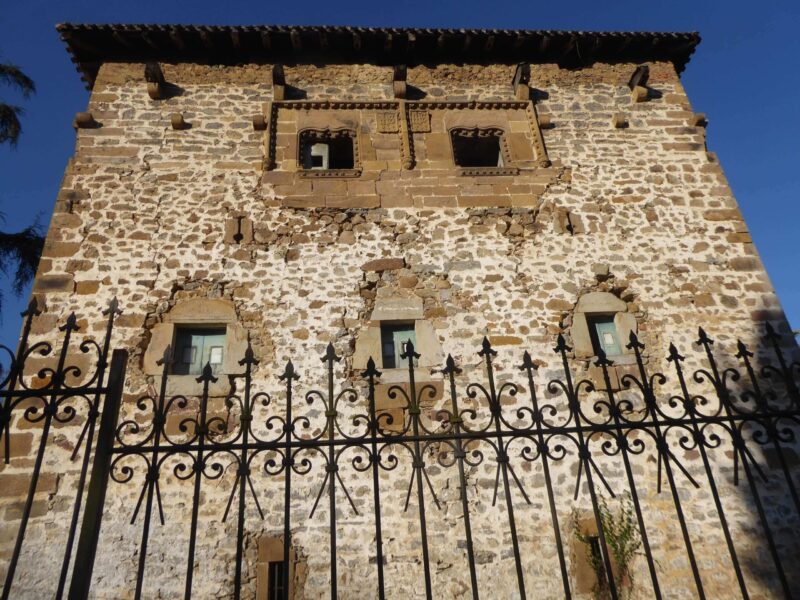 Edificio defensivo de piedra con ventanas muy decoradas en la parte alta y reja de cierre en la parte baja