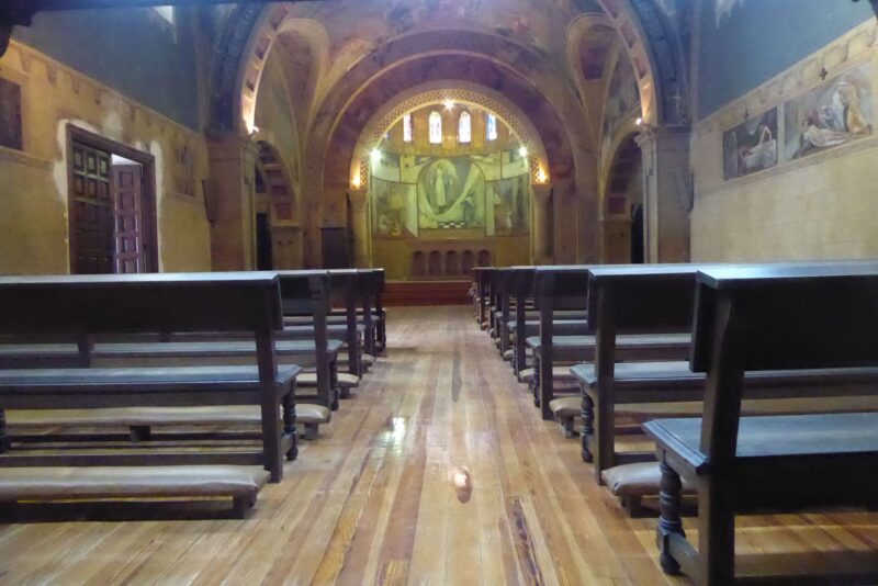 Interior de una capilla con frescos en las paredes y bancos en el medio