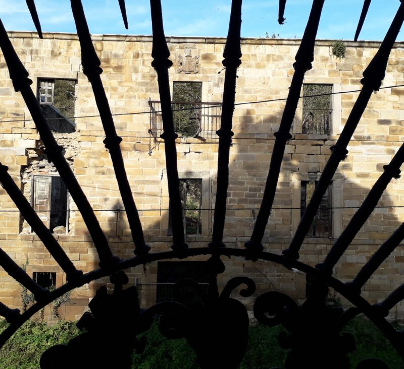 Fachada de un edificio en ruinas vista a través de una verja con forma de rayos de sol